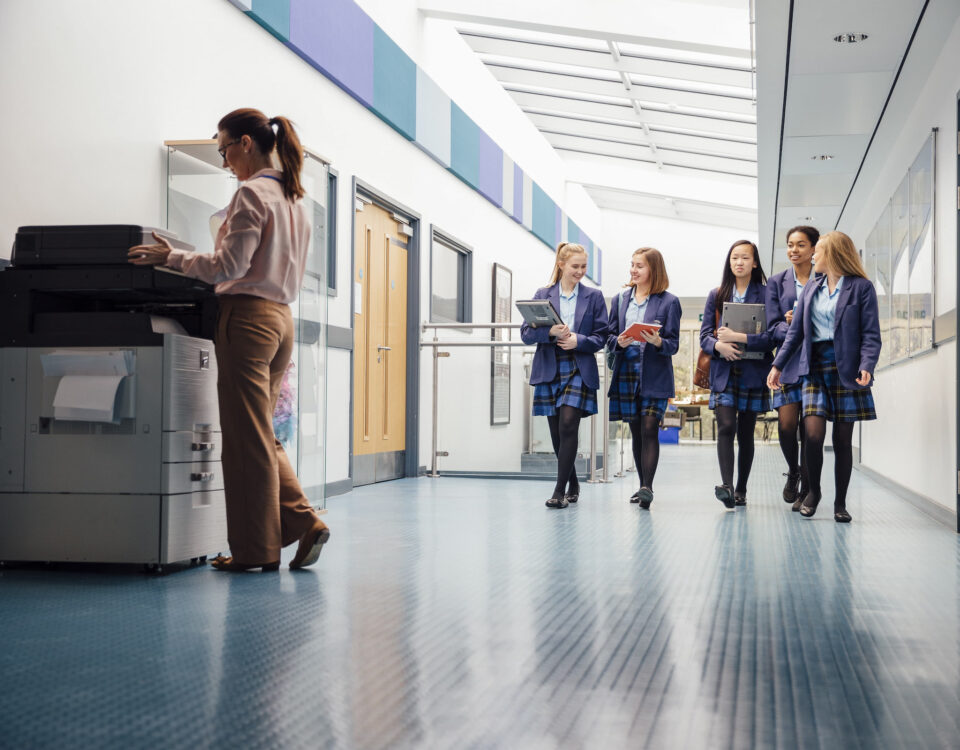school girls in school hallway with adult woman using hp printer photocopier
