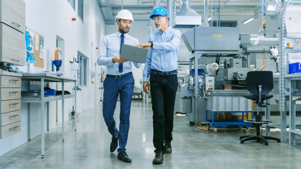 two men in manufacturing industrial plant reviewing laptop