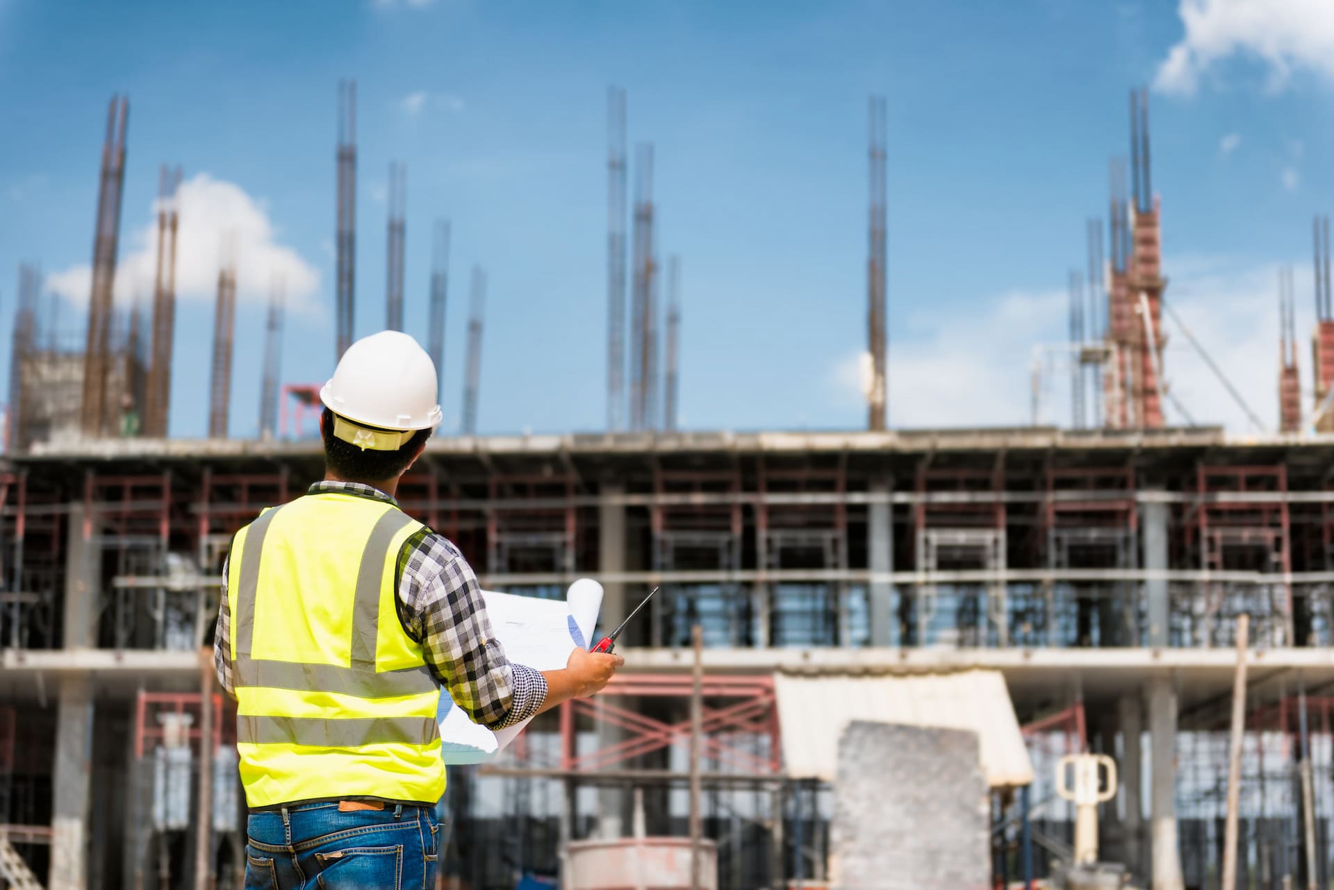 construction worker yellow vest blueprints building scaffolding blue sky