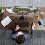 overhead man in suit sitting at wood desk HP laptop curved monitor