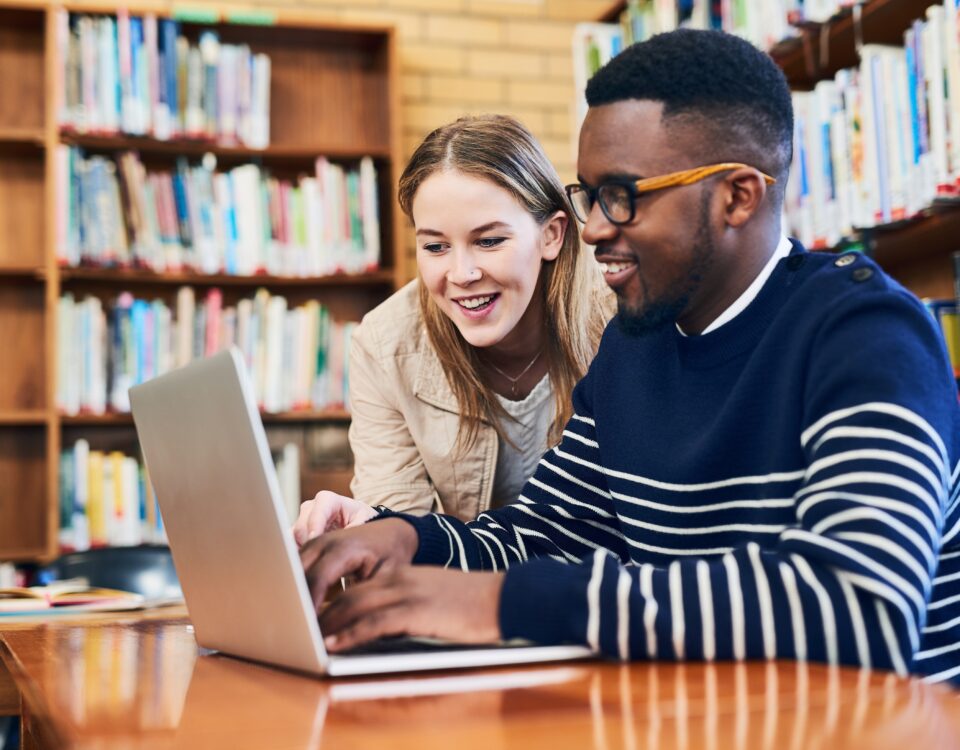 students in a library working on a laptop