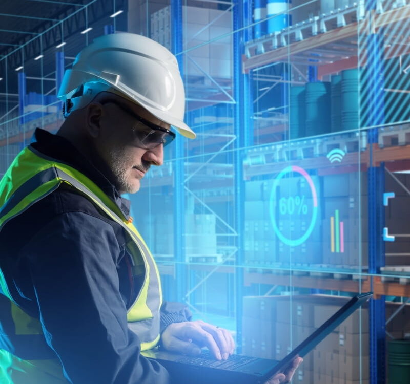 yellow vest warehouse worker using laptop to digitally manage inventory